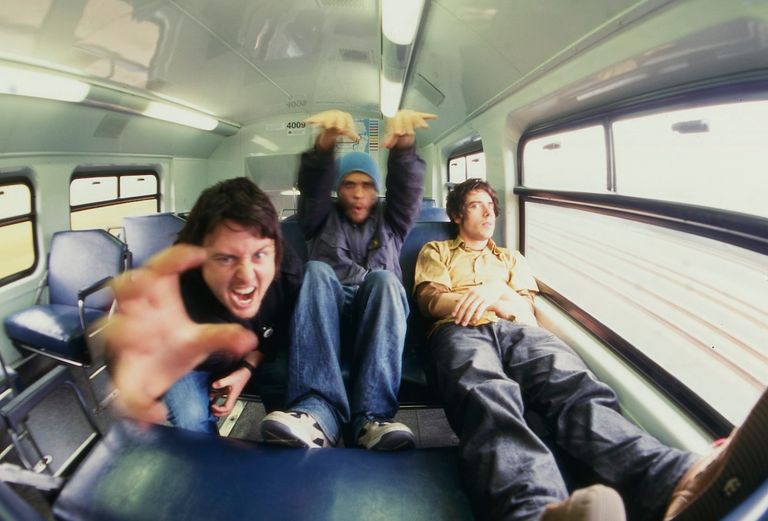 Candid wide-angle shot of Australian band Gerling fooling around inside a train carriage, sitting on blue seats.